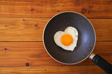 Heart shape fried egg in the pan on wooden background. top view. Valentine's day celebration. healthy food  concept. 