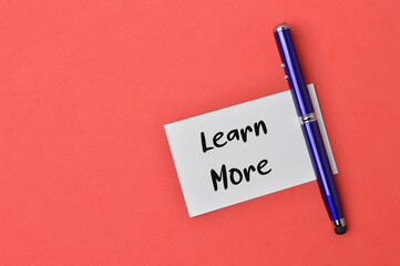 Top view of pen and memo note written with text LEARN MORE over red background. Business and education concept.