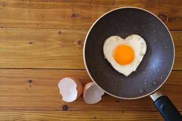 Heart shape fried egg in the pan  with egg shell on wooden background. top view. Valentine's day celebration. healthy food  concept. 
