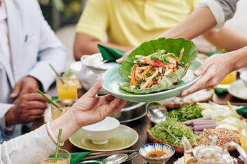 Close-up image of housewife giving plate with delicious seafood salad to guests at dinner