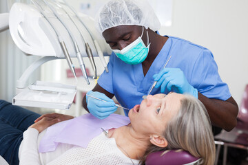 Mature female patient sitting in dental chair. Dentist is treating female patient