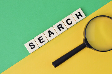 Top view of magnifying glass and scrabble letters with text SEARCH over green and yellow background.