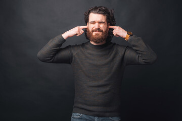 An upset young man is covering his ears because is too noisy there .