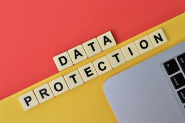 Top view of laptop and scrabble letters with text DATA PROTECTION over yellow and red background. 