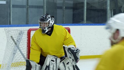 Hockey goalie in protective gear and sports uniform protecting gate during game on ice rink - Powered by Adobe