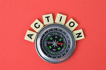 Top view of compass and scrabble letters with text ACTION over red background. 