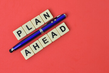 Top view of pen and scrabble letters with text PLAN AHEAD over red background. 
