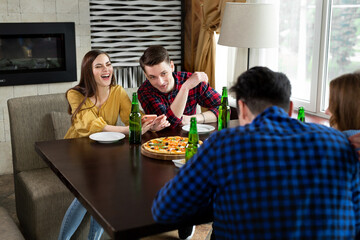 Group of young friends with pizza and bottles of drink celebrate in a cafe