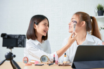 Two young Asian woman beauty vlogger video online is showing make up on cosmetics products and live video on digital digital camera.