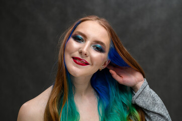 Fototapeta premium Photo of a happy woman. Portrait of a beautiful caucasian girl with dyed hair and excellent makeup on a gray background.
