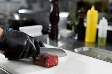 Chef in hotel or restaurant kitchen cooking, only hands, he is cutting meat or steak