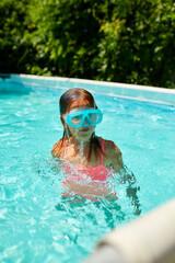 A cute happy young girl child playing in swimming pool wearing blue diving mask