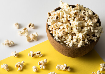 Popcorn in a wooden bowl on a yellow background