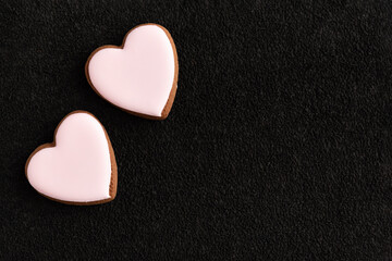 Two white glazed heart shaped cookies on black background. Copy space.