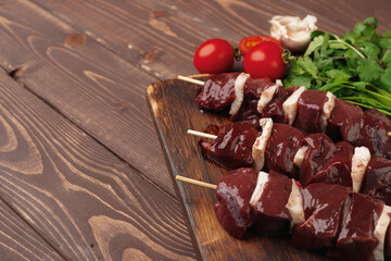 Raw beef liver kebab on skewers on wooden board