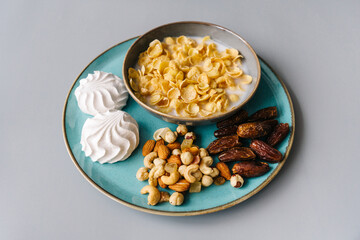 Bright breakfast on gray background, front view. Tasty flackes, nuts, marshmallows and dates.