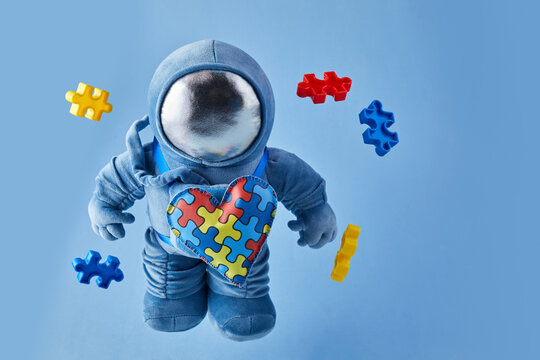 World Autism awareness day background. Blue plush astronaut toy with puzzle heart, autism symbol, on blue background