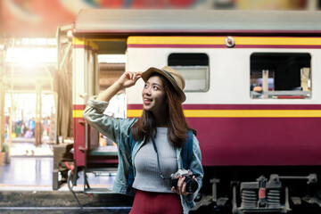 Smiling happy young Asian backpacker female standing at train station with sunshine effect. Travel and vacation lifestyle concept.