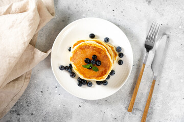 Pancakes in a white plate on the light gray kitchen table. Homemade delicious pancakes with honey...