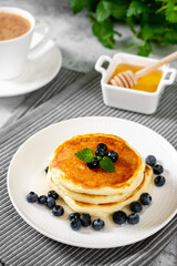 Pancakes in a white plate on the light gray kitchen table. Homemade delicious pancakes with honey and blueberries. Delicious sweet and hearty breakfast	