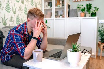 Young handsome businessman working in modern living room using laptop. Remote work from home