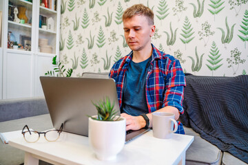 Young handsome businessman working in modern living room using laptop. Remote work from home