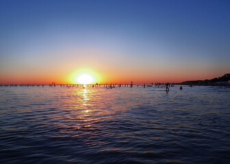 sunset on the sea, a resort town with a pier, silhouettes of vacationing people on the sea