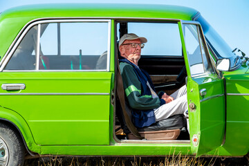 Old man with glasses in the car. In the passenger seat. The door is open.