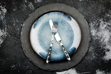 Black round slate board with cutlery on dark stone texture top view. Place for a menu or recipe