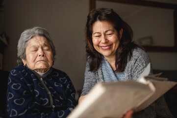 Old sick woman with memory loss. Smiling daughter showing a photo album