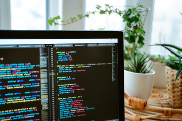 St Petersburg, Russia - 30 Jan 2021: Html code on the laptop screen standing on a wooden table with home green plants, cozy working office. Selective focus