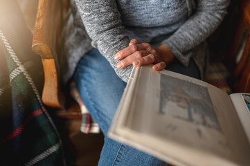 Close-up unrecognizable woman holding a photo album sitting on the sofa. Memories concept