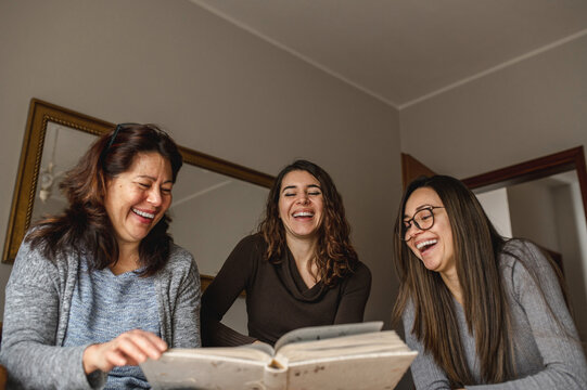 Frontal view three women, mother and daughters looking a book of memories. Togetherness, family, positive emotion concept.