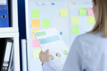 Woman holding documents with charts in front of board with stickers