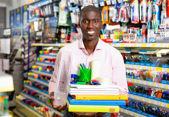 African american positive smiling male customer choosing paper office supplies in stationery shop