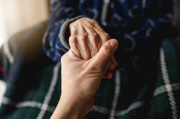 Unrecognizable young person holding hands of old woman. Elderly, care, family concept