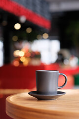 A small black coffee cup on a saucer on a wooden table. Coffee in a cafe on the background of blurred background