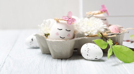 Easter holiday concept with cute handmade white eggs, tree branches, quail feathers and spring flowers on white wooden background.