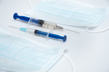 Two syringes with different dose of medicine or vaccine with two protective face masks on white or gray background with place for the text: vaccinations against influenza coronavirus