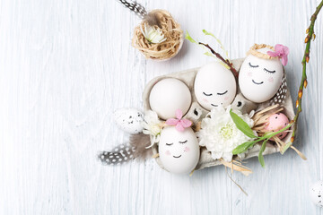 Easter holiday concept with cute handmade white eggs, tree branches, quail feathers and spring flowers on white wooden background.