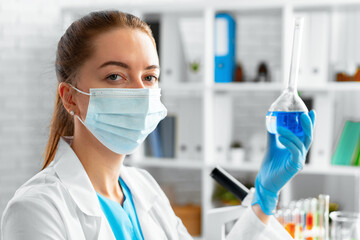 Woman scientist or laboratory worker holding glass flask with chemical liquid