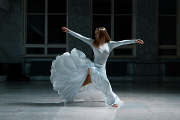 choreography from a beautiful girl in a white dress, a wooden floor, a dark room with large windows.
