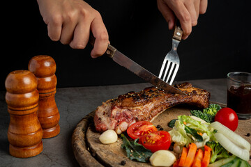 Young woman eating grilled pork steak and vegetables on wooden cutting board