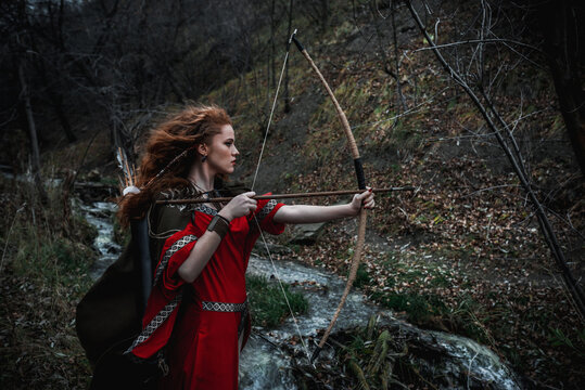 Red-haired woman in a red dress in a historical Celtic costume in the autumn forest