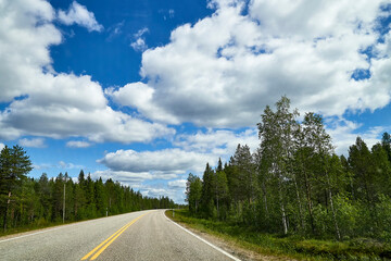 View from relief car windscreen on the blue sky with white clouds, grey asphalt road and landscape with forest and green teeses. Landscape through window