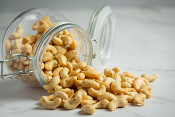 Raw cashews nuts in an open glass jar on marble background