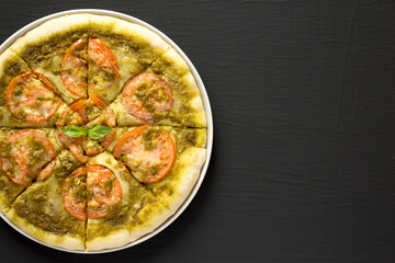 Homemade Pesto Pizza with Fresh Tomatoes and Mozzarella on a black background, top view. Flat lay, overhead, from above. Space for text.