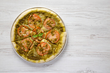 Homemade Pesto Pizza with Fresh Tomatoes and Mozzarella on a white wooden surface, top view. Flat lay, overhead, from above. Copy space.