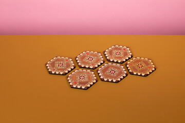 Vintage marquetery coasters with brown and beige colors. An eclectic oriental pattern made from mosaic wood on an ochre table and a pink background