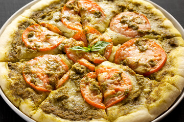 Homemade Pesto Pizza with Fresh Tomatoes and Mozzarella on a black background, low angle view. Close-up.